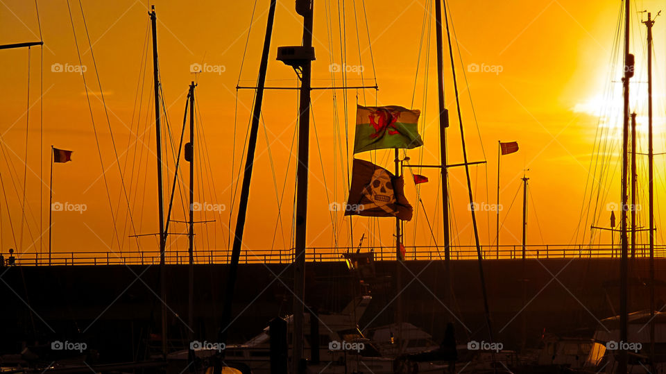 Beware of Welsh pirates in the port. Baner of Wales and pirates scull and bones flag weaving on wind during the sunset. Wales. UK. Cymru.