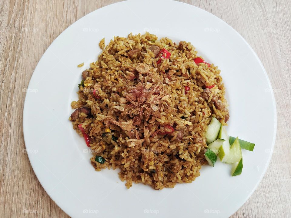 Goat fried rice on a white plate, topped with fried onions and cucumber slices. Delicious spicy taste. Indonesian food