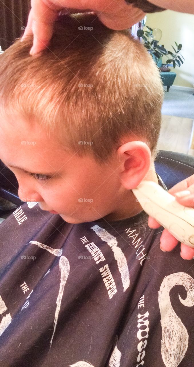 Barber cutting little boy hair with trimmer