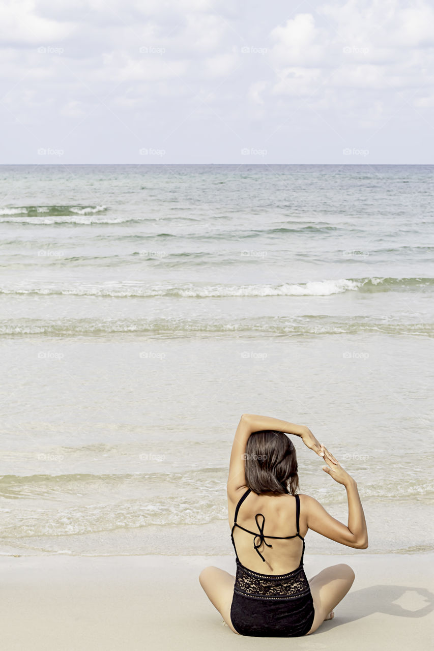 Portrait of Asian woman wearing a swimsuit sitting yoga on the beach background sea and sky