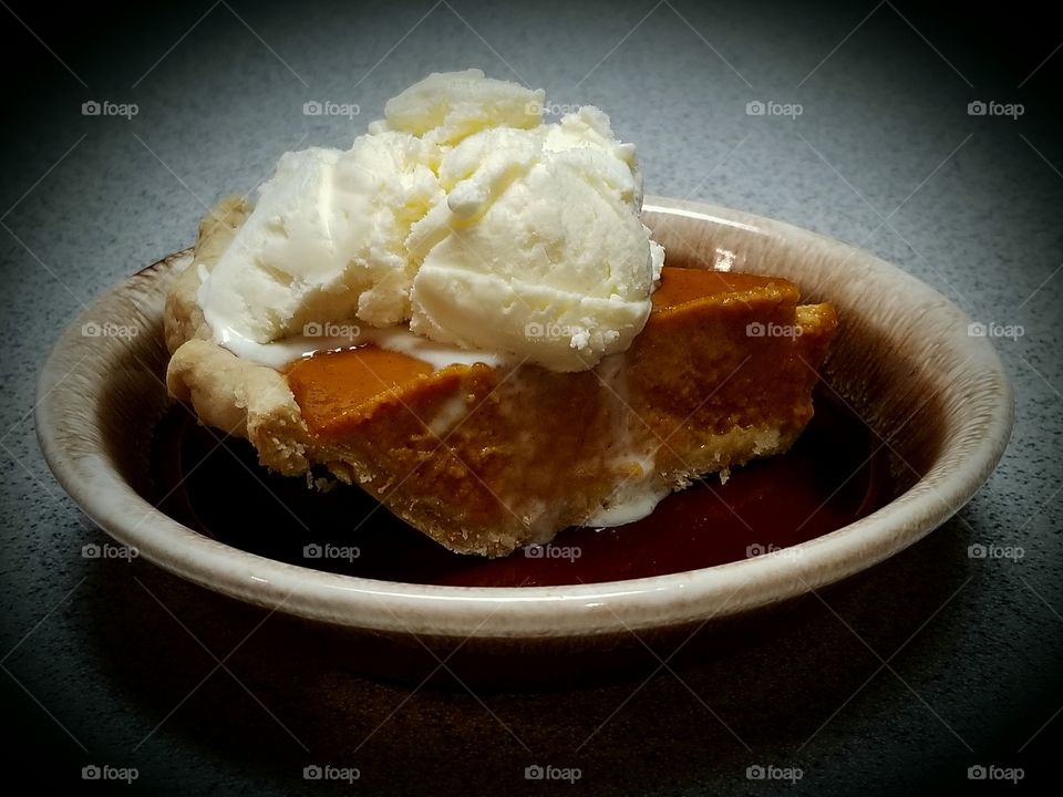 Warm homemade pumpkin pie served with vanilla ice cream on a rustic brown drip plate