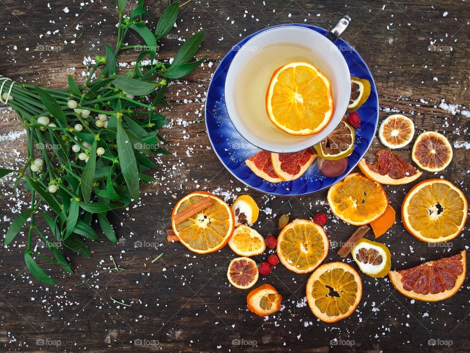 Mug of orange tea and cinnamon with dried orange slices beside and mistletoe on snowy table