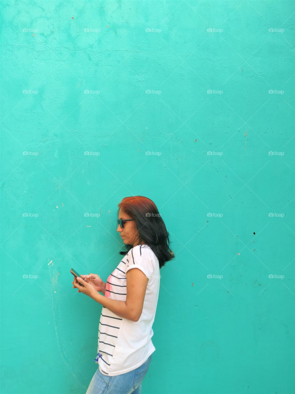 woman standing against a solid green wall and using her smartphone