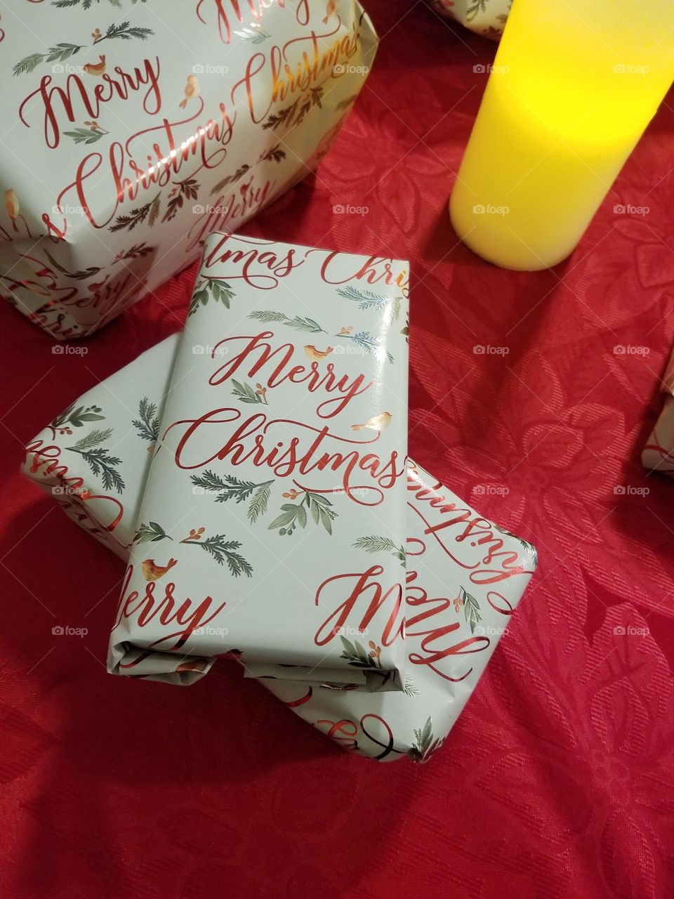 Wrapped Christmas presents sitting on a red tablecloth with a candle. Gift wrapping station. 🎁