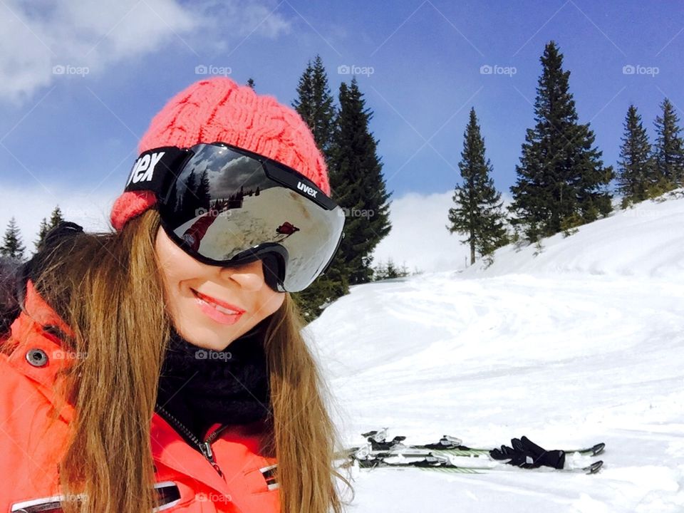 Selfie of woman with ski glasses on and skis in the background