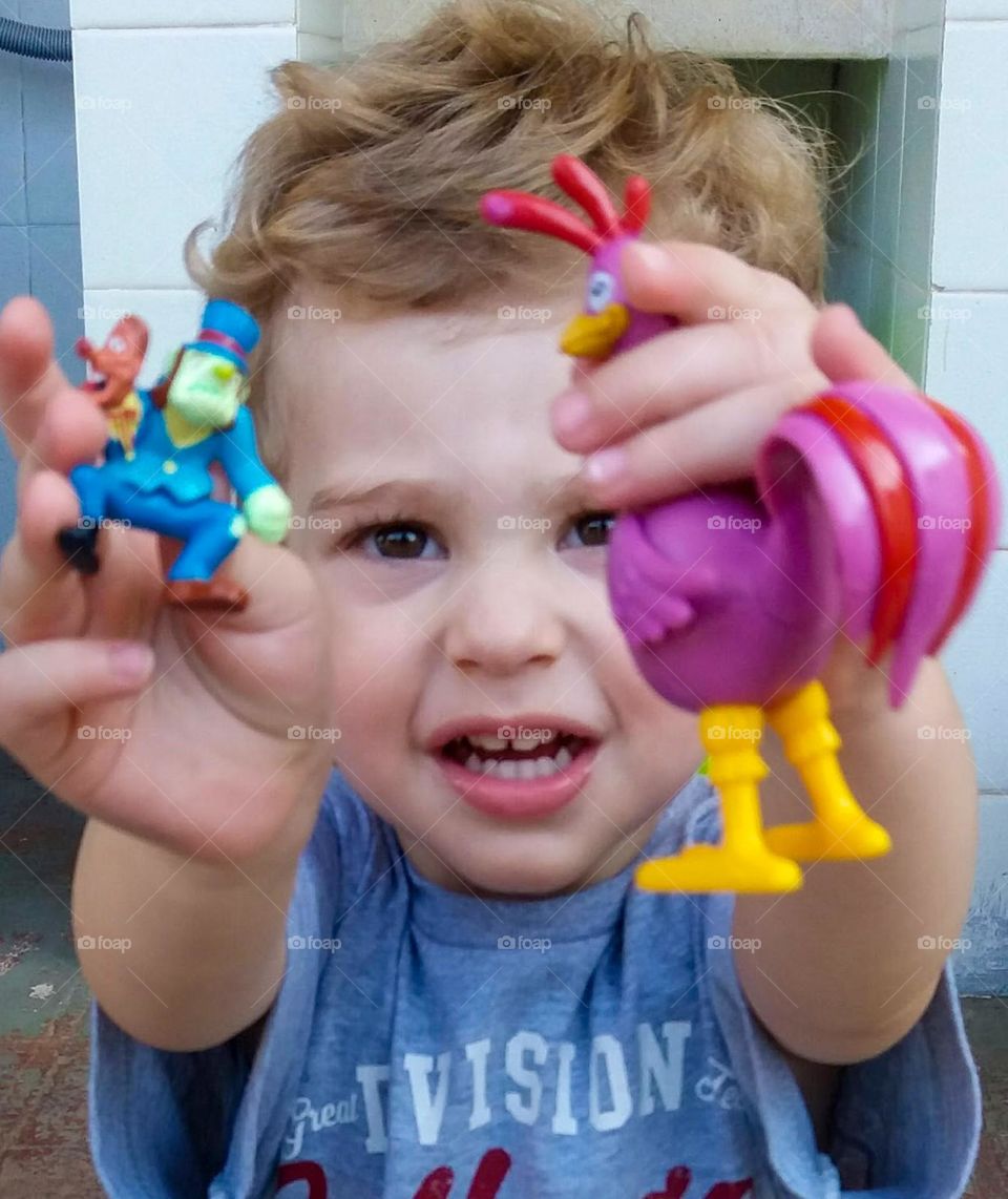 child with two colorful toys, one of them in purple, calling the mother to play.
criança com dois brinquedos coloridos, sendo um deles na cor roxo, chama a mãe para brincar.