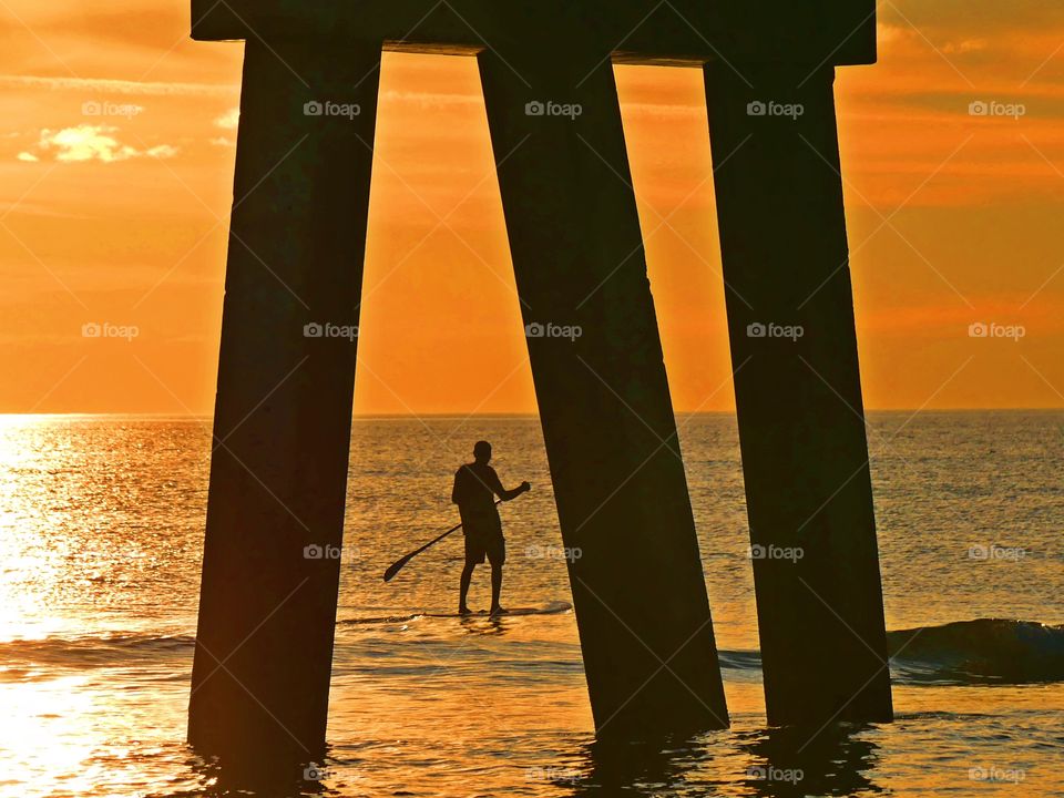 Man paddle boarding between the pier - Silhouettes are a wonderful way to convey drama, mystery, ... The perfect light for this is placing your subject in front of a sunset or sunrise – but really any bright light will be.