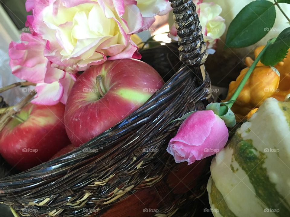 Fresh apples in basket with pink garden roses and autumn harvest gourds on table decorative centerpiece still life photography 