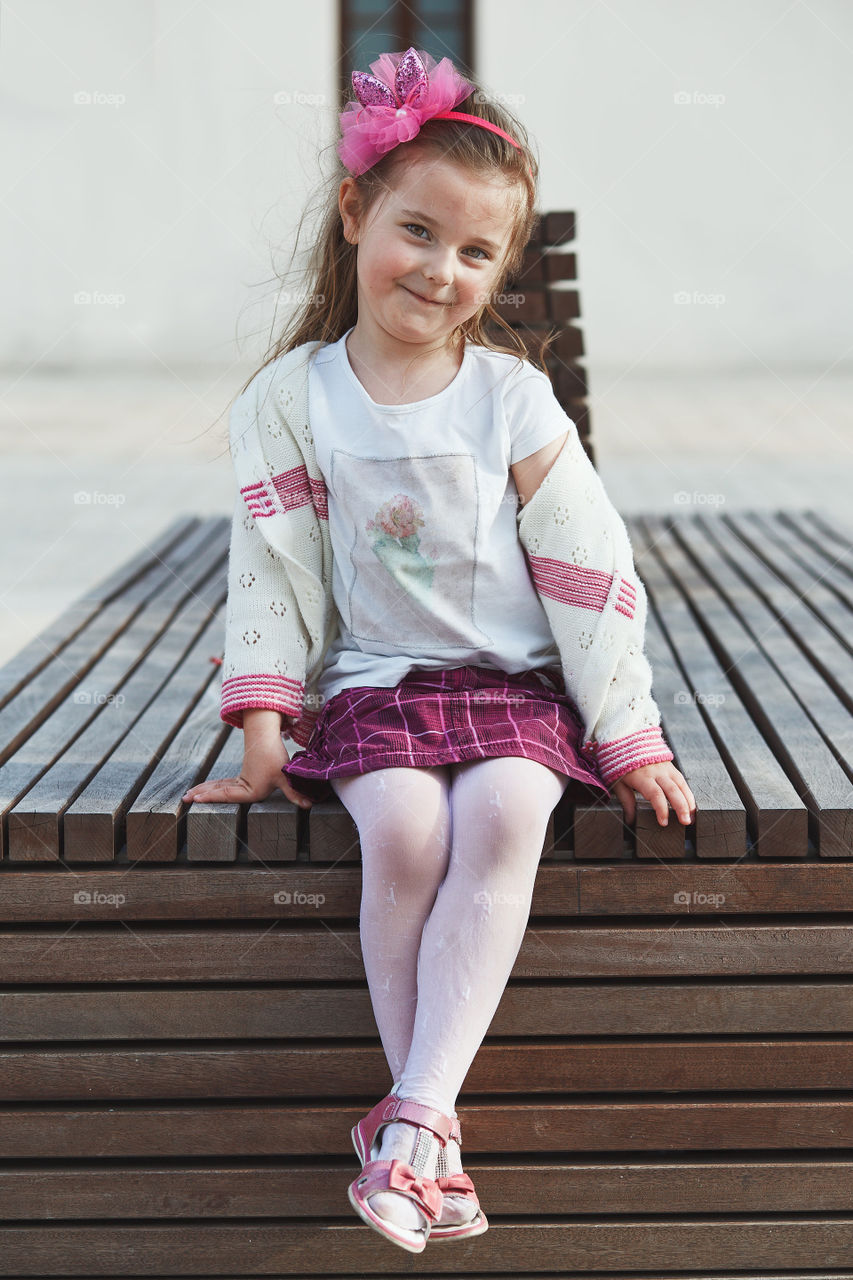 Portrait of cute adorable little girl sitting on bench in the center of town