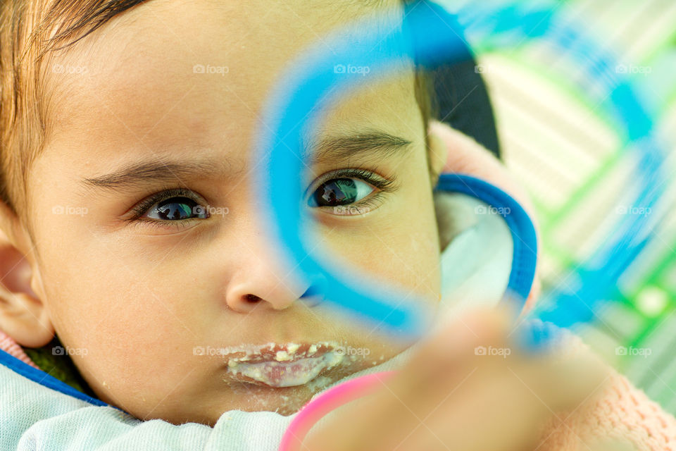 Little baby eating food, having food all over his face. Playing with a toy.