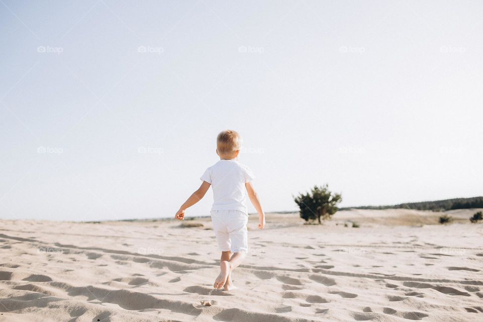 Small boy in white clothes running in desert