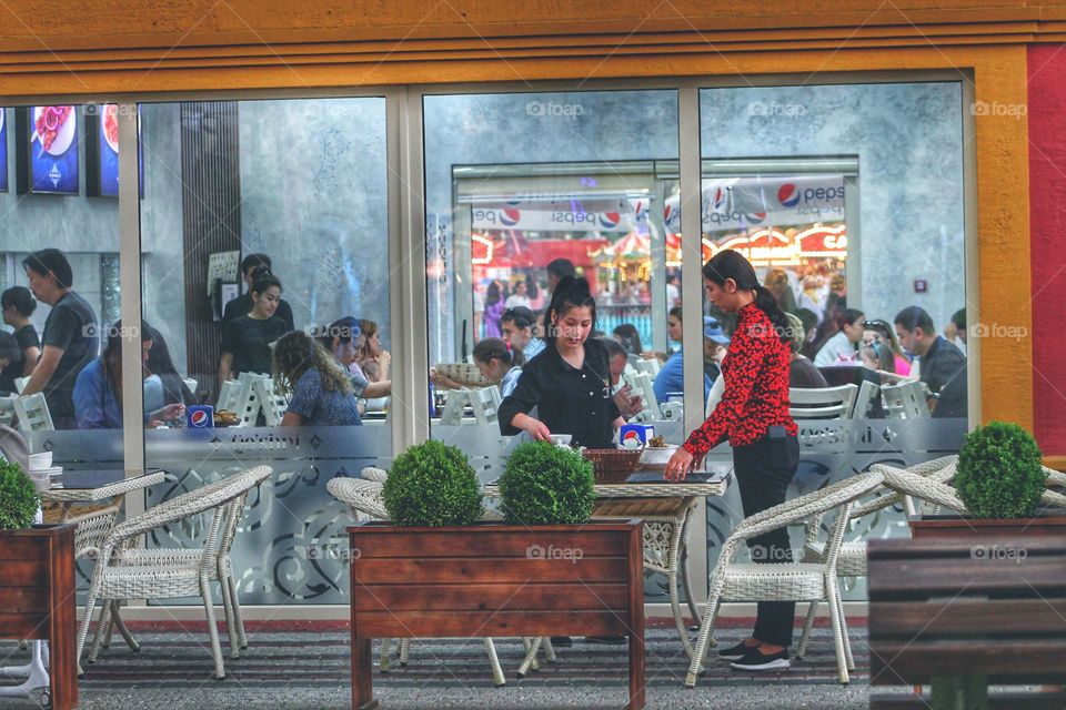 the waiters in the cafe set the table. cafe with huge windows to the floor also has beautiful flower beds with plants.