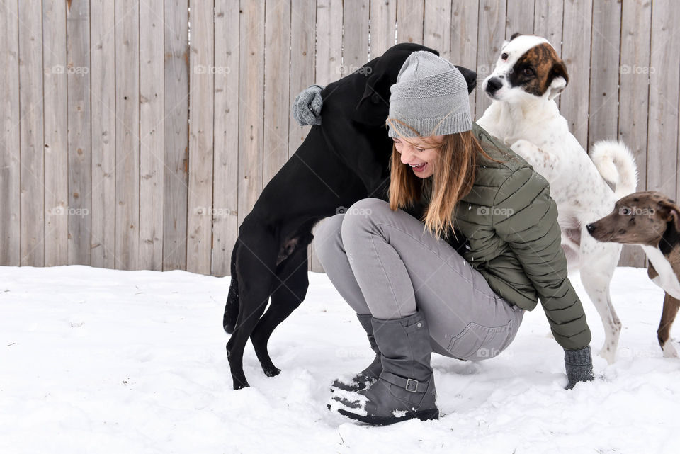 Young woman laughing and playing with her dogs outdoors in the snow