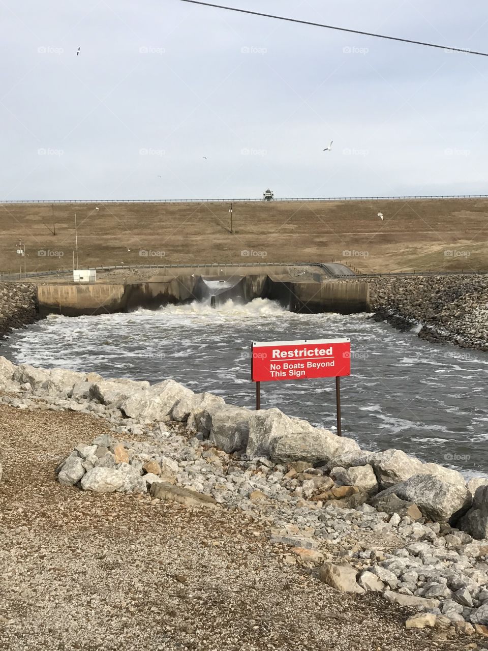 US Army Corps of Engineers OOlogah Lake Dam, Oologah, Oklahoma winter January water release area with sign identifying restricted area, seagull birds fishing by flood gates, rip rap rocks along water channel