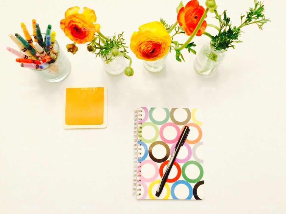 Desk From Above. Another overview of my workspace with colored pencils, a notebook, and fresh Ranunculus blooms