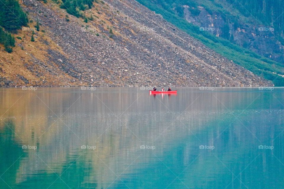 People in red canoe at dawn on turquoise Lake reflecting on the water (Lake Louise in Canada's Rocky Mountains) 