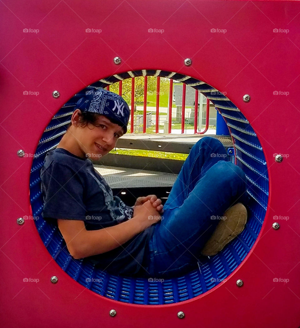 teenaged boy sitting in a red and blue playground tunnel