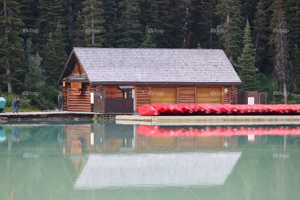 Wood log cabin style boathouse and its reflection at Lake Louise in the Rocky Mountains of Alberta near Banff, red kayaks and boathouse reflections 