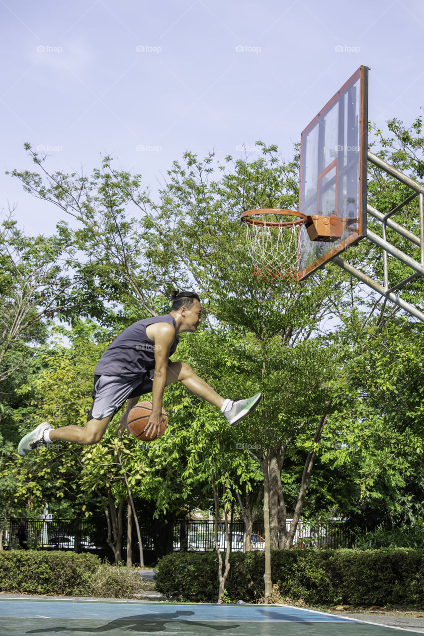 Basketball in hand man jumping Throw a basketball hoop Background  tree in park.