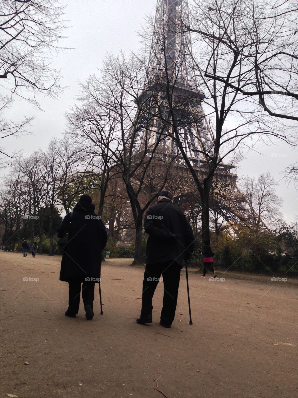 An elderly couple takes a walk together by the Eiffel Tower. Old friends or longtime lovers?