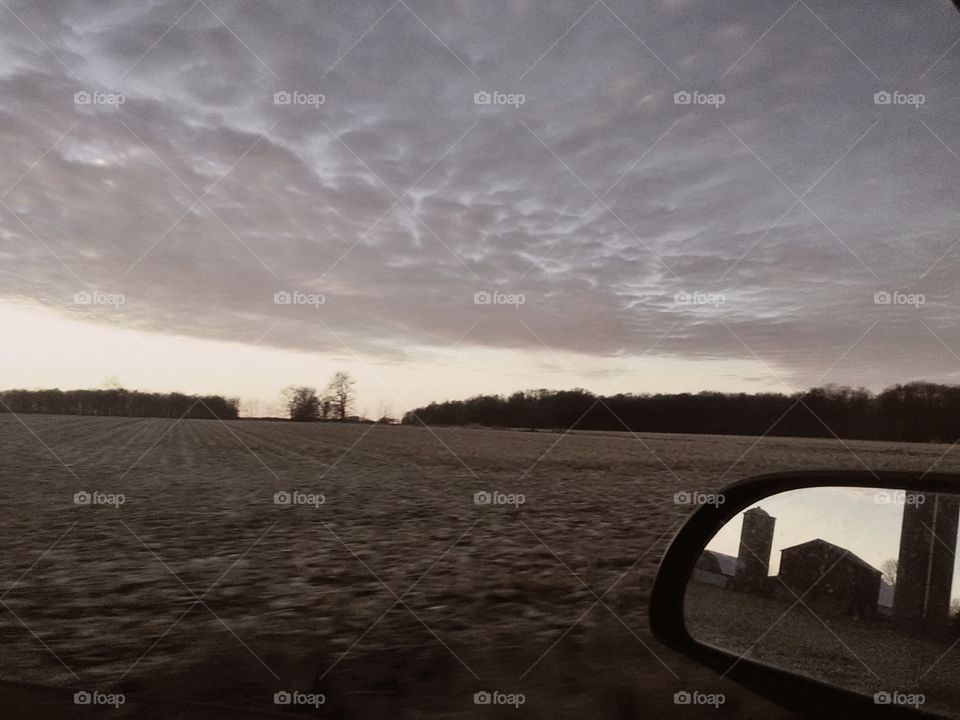 black and white of rural farmland under a sheet of clouds and reflection in car mirror