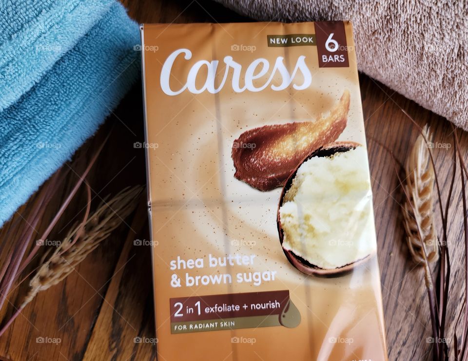 The new look Caress bar soap shea butter and brown sugar six pack,  next to a tan towel and light blue towel on a wood surface.
