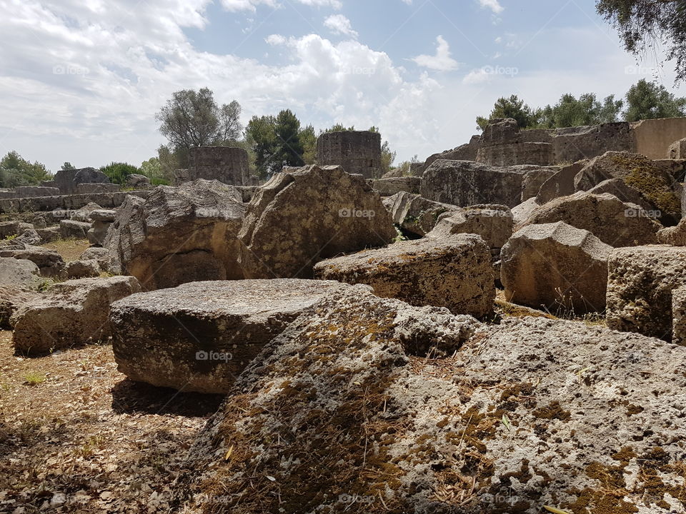 Fallen marble pillars of ancient Greece in Olympia, ruins of historical site on sunny summer day