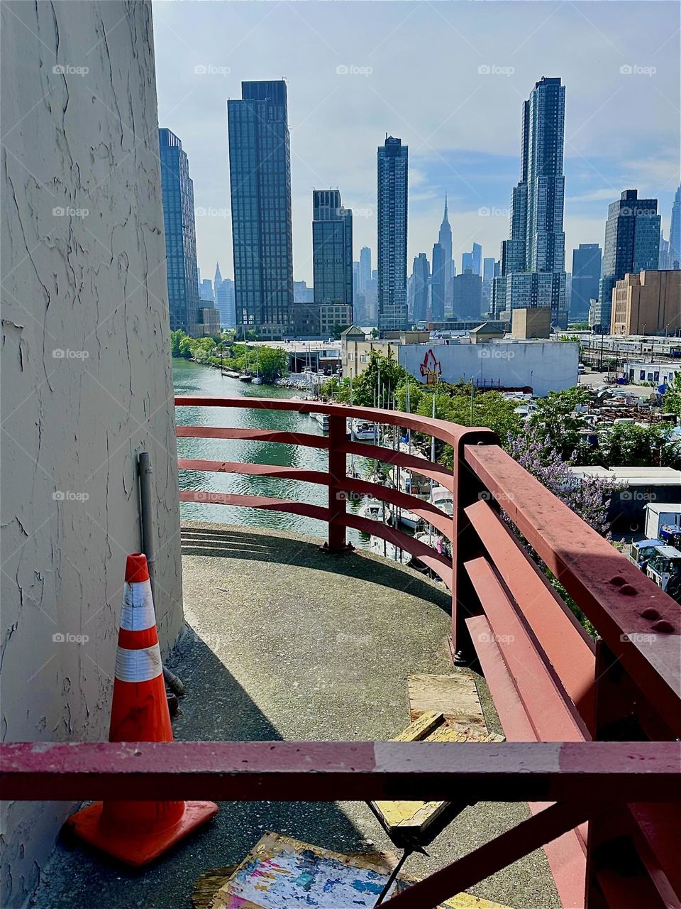 This is “Newtown Creek” seen from the center outpost of the “Pulaski Bridge” that connects “Greenpoint”, Bklyn to LIC, Queens. Across the “E River” in the distance we see “Manhattan” including the “Empire State Building”. 2024. Hypnotic Productions