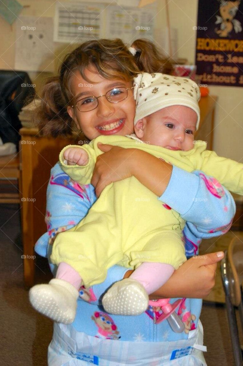 Girl holding her baby sister. . Young girl holding her baby sister at a Halloween party at a grade school .