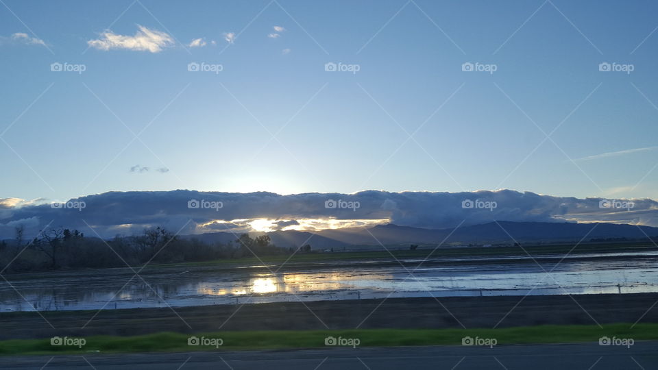 drivung down HWY 5 after a day of rain. sun setting behind the mountainswith the last rays of the sun shining and stretching across farm fields.