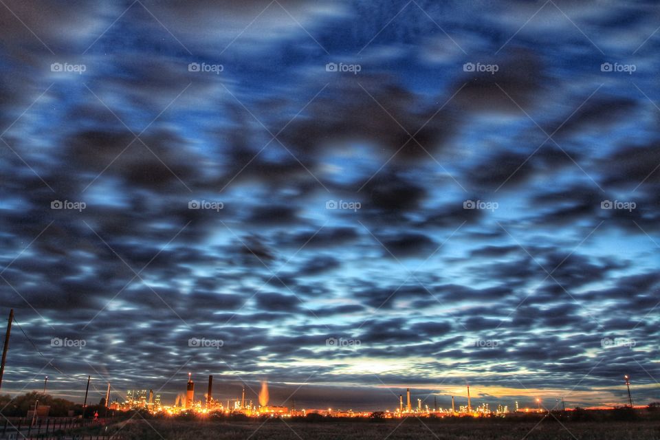 Colourful skies. An oil refinery lit up at night below a colourful, dark sky.