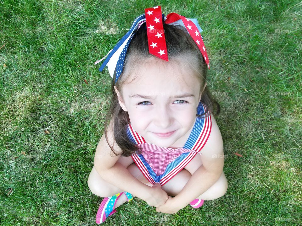 4th of July. Little girl dressed in red, white and blue sitting in the grass. 