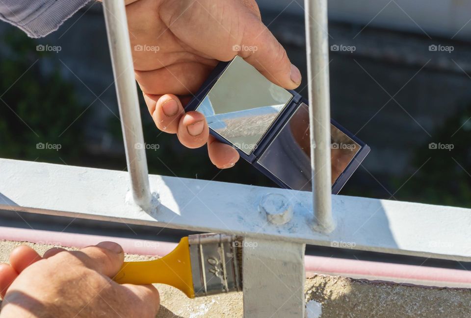 The craftsman paints the fence and uses a mirror to check the non-visible side