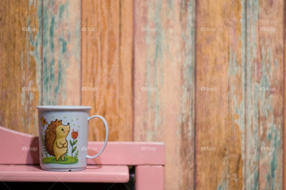 Cute mug with the image of a hedgehog on a wooden background. Kitten utensils 