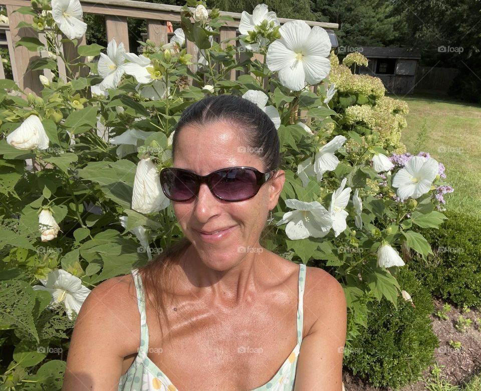 Closeup of woman in sundress snd sunglasses in front of white flowers