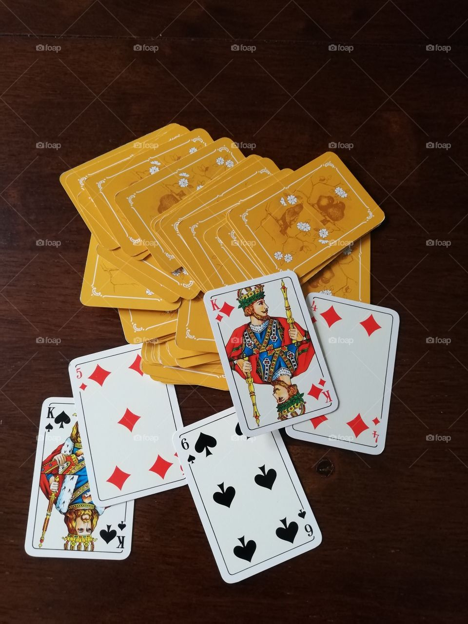 The pack of playing cards is spread around on the brown table, five sides up: two spades and three diamonds. The rest of them faces down. The backs are figured with birds and flowers.