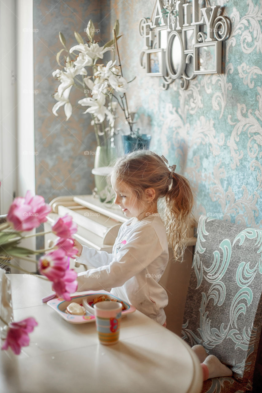 Little girl eating her breakfast in a light kitchen 