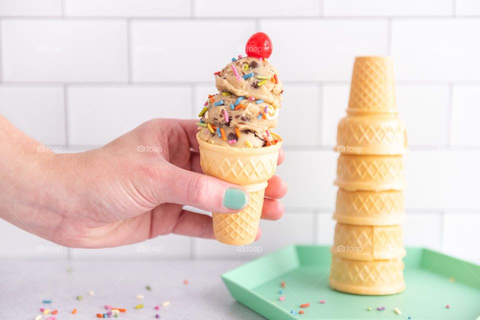 Person’s hand holding an ice cream cone with sprinkles and a cherry on top in the summer 