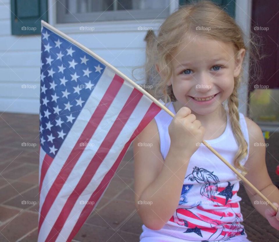 Beautiful little girl with braided pigtails, proudly holding the American flag. 