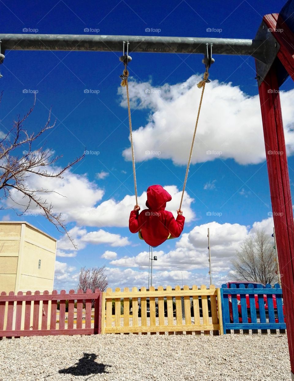 one boy swinging with a red jacket in a cold day with a blue Sky and clouds