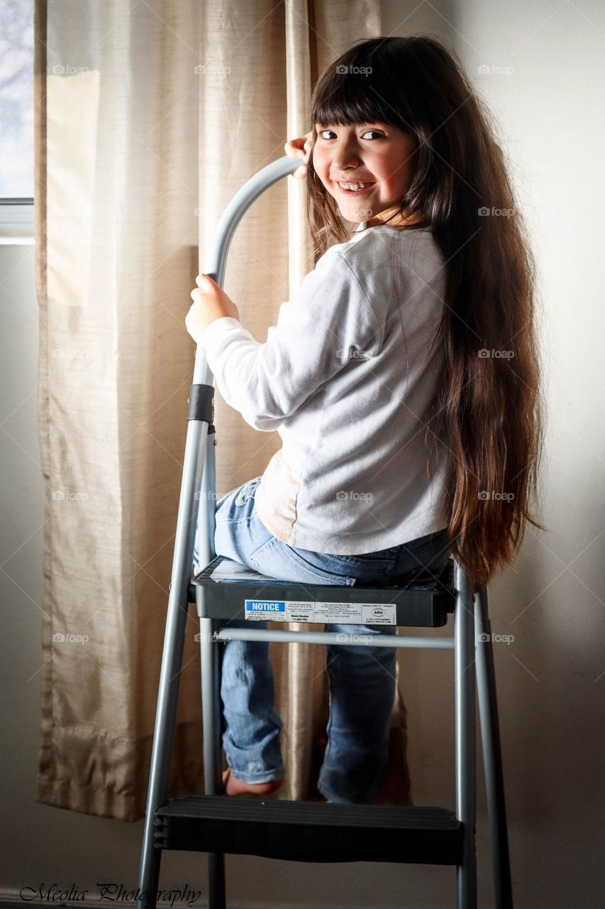 Cute happy girl with a long hair is sitting on a step ladder