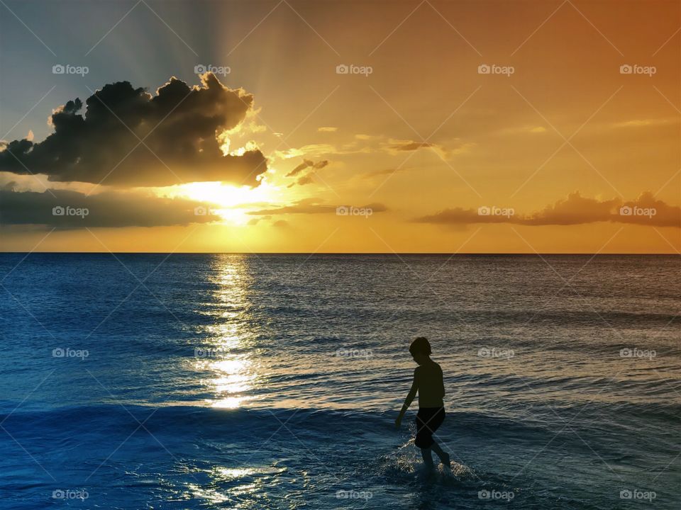 Small boy in the ocean under a gorgeous golden sunset.