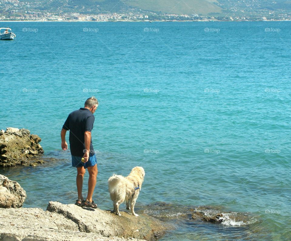 Old man and his dog play with a tennis bell at sea.
