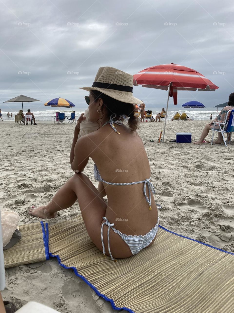 Menina descansando e apreciando a beleza da praia. Protegida com chapéu.