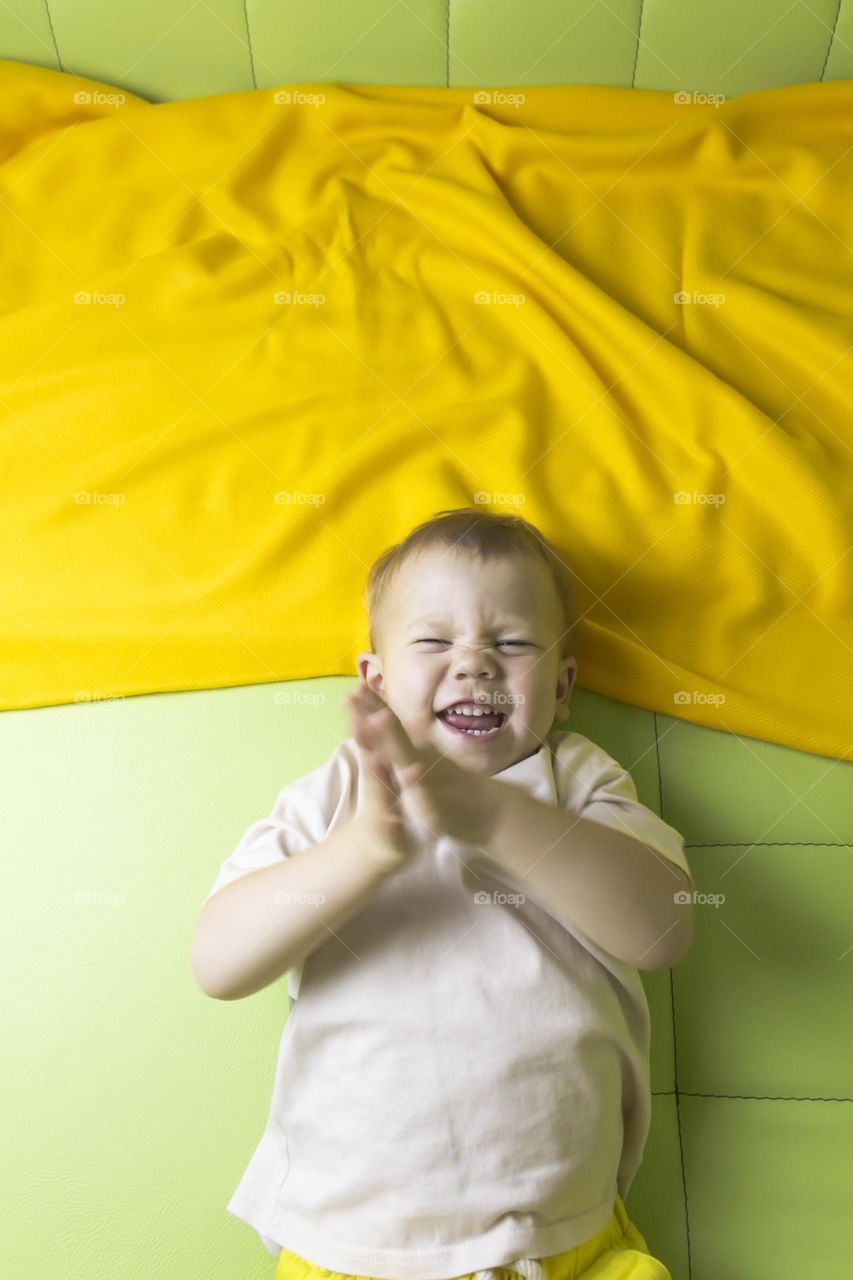 A portrait of a child sitting at home on a green sofa depicts different emotions in yellow shorts.