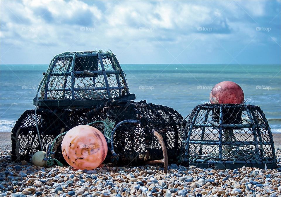 Lobster pots and bright orange buoys sit on the pebbled beach at St Leonards on sea, UK 