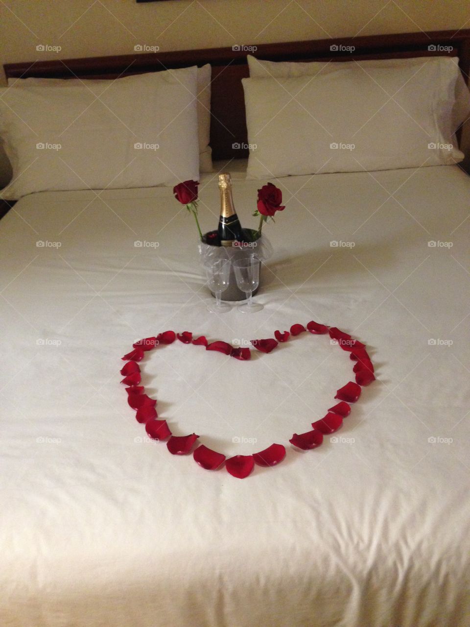 Flower petal heart on a bed with champagne and roses