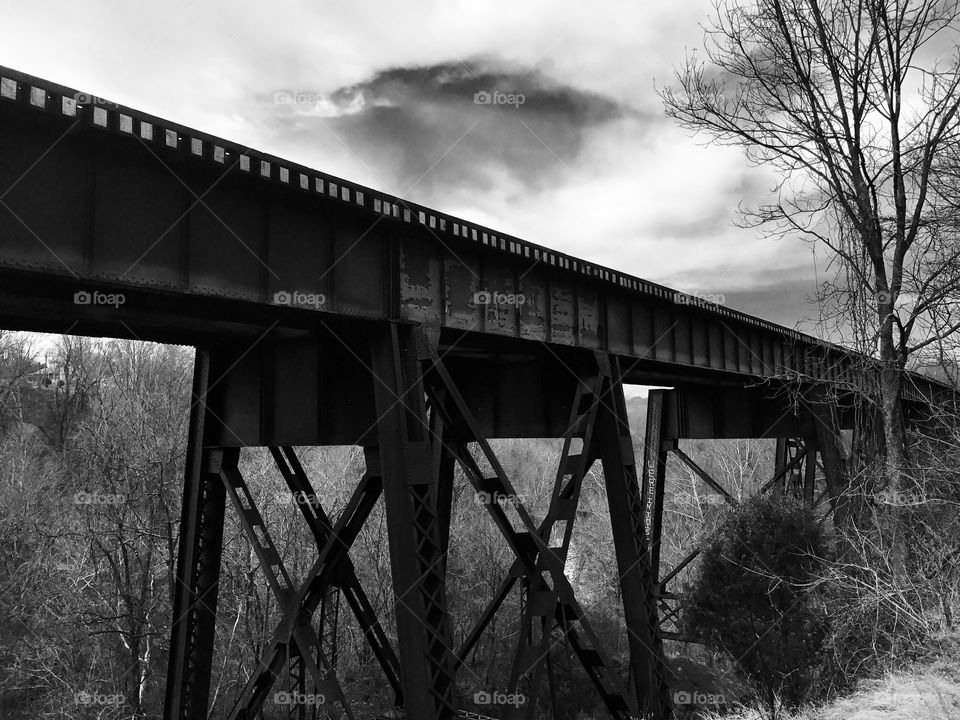 Clouds over trestle bridge, over pathway, over a creek. 