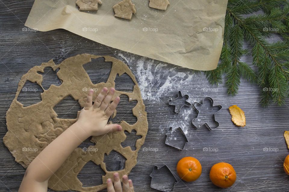 A small child helps to prepare festive, gingerbread cookies on a wooden table on Christmas Eve.