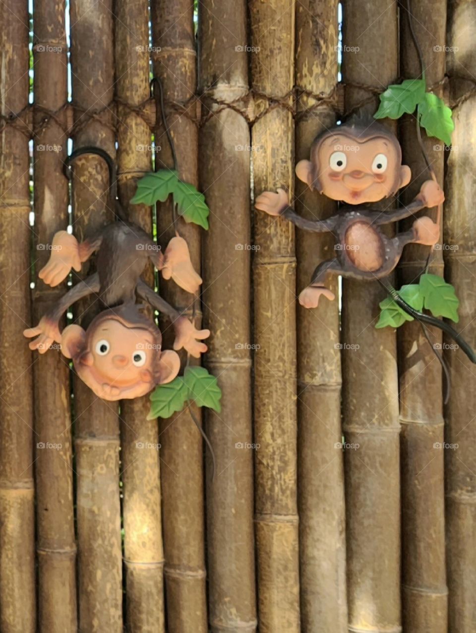 Metal Art Decoration of silly funny jungle monkeys on brown bamboo fence in garden yard, summer day